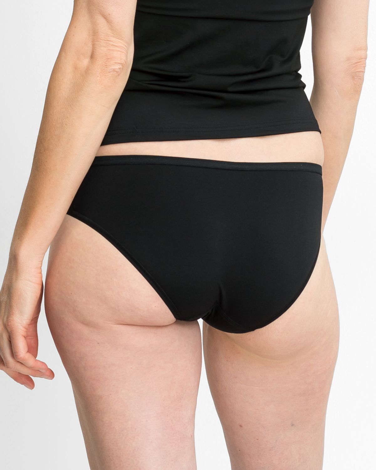 Model trägt Bikinislip in schwarz aus der Serie Sidney, Ansicht von hinten.