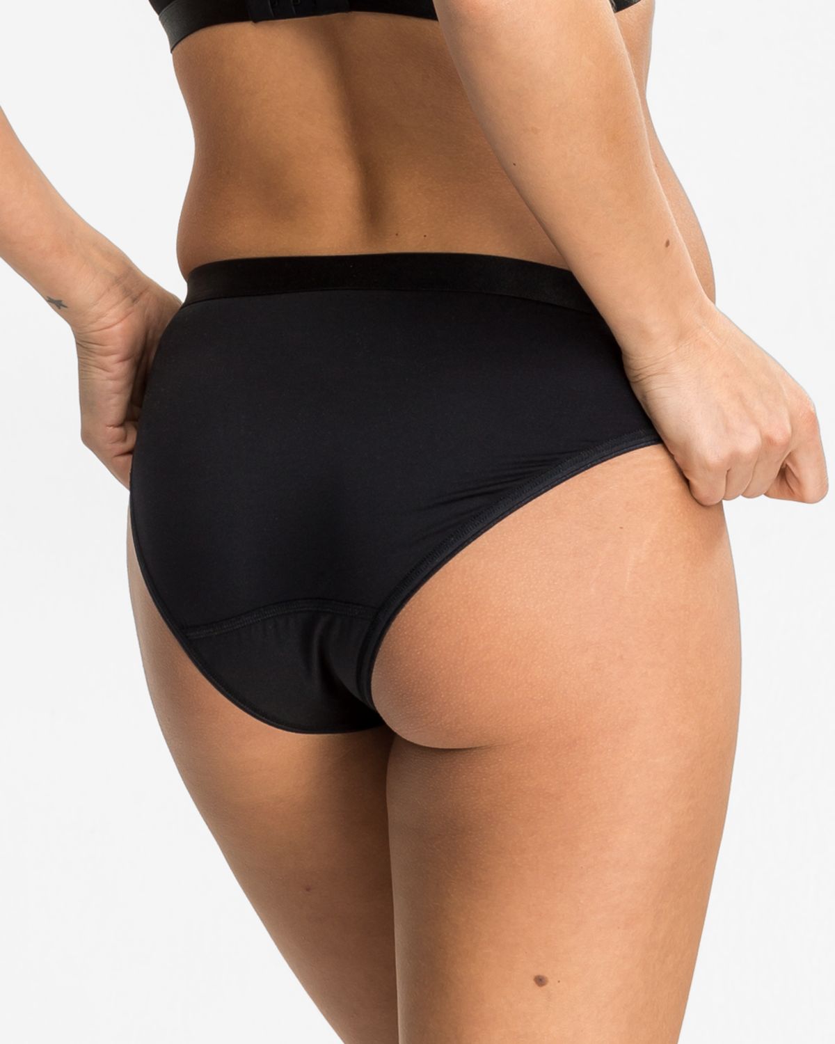 Model trägt Bikinislip in schwarz aus der Serie Priscilla, Ansicht von hinten.