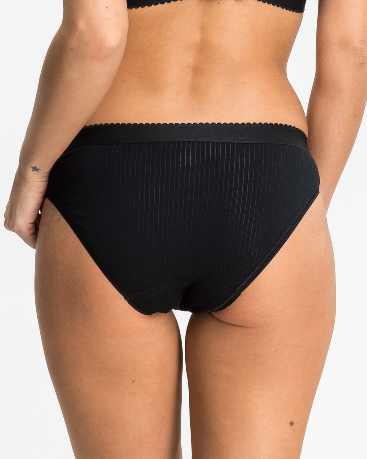 Model trägt Bikinislip in schwarz aus der Serie Palina, Ansicht von hinten.