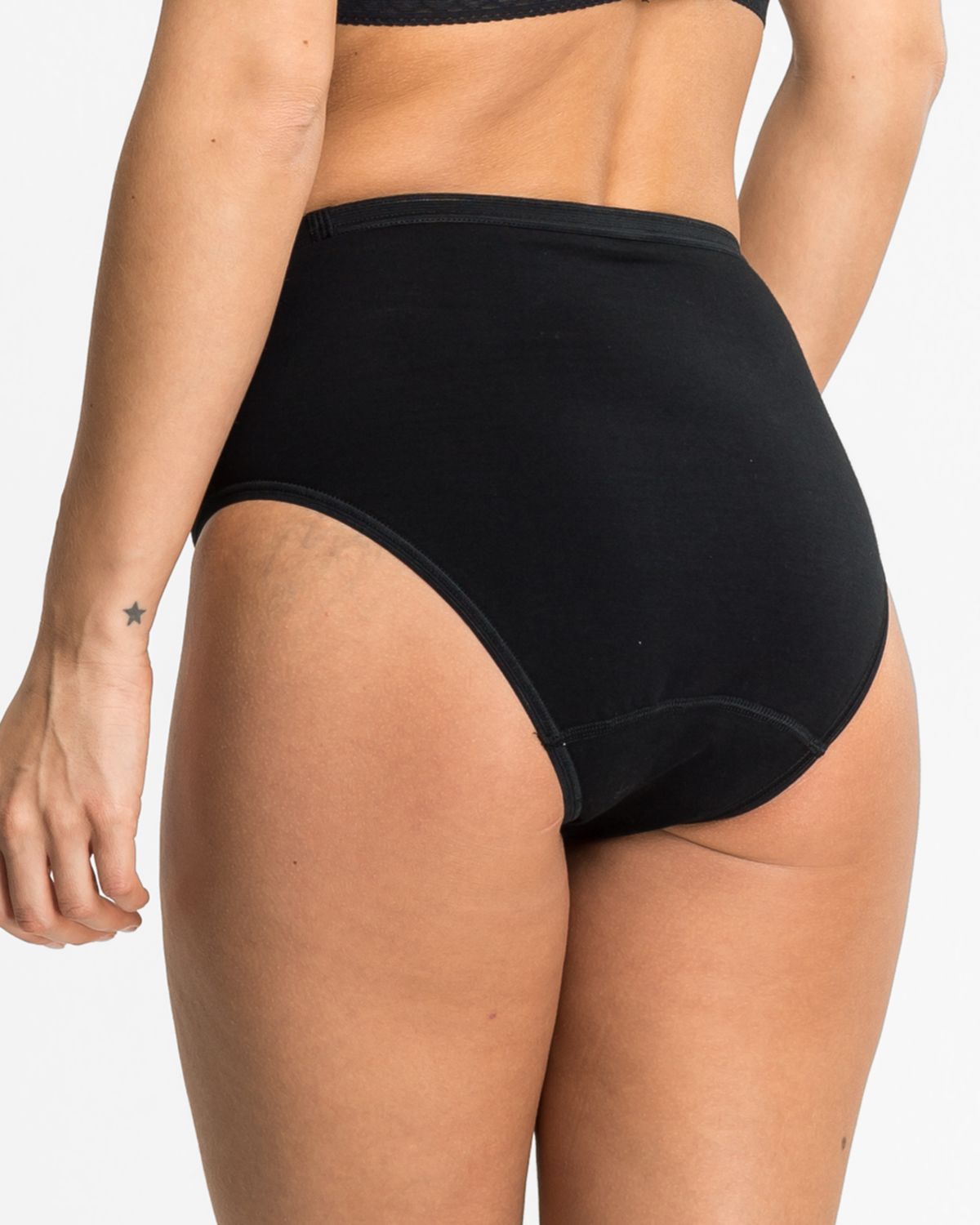 Model trägt Hüftslip in schwarz aus der Serie Britta, Ansicht von hinten.