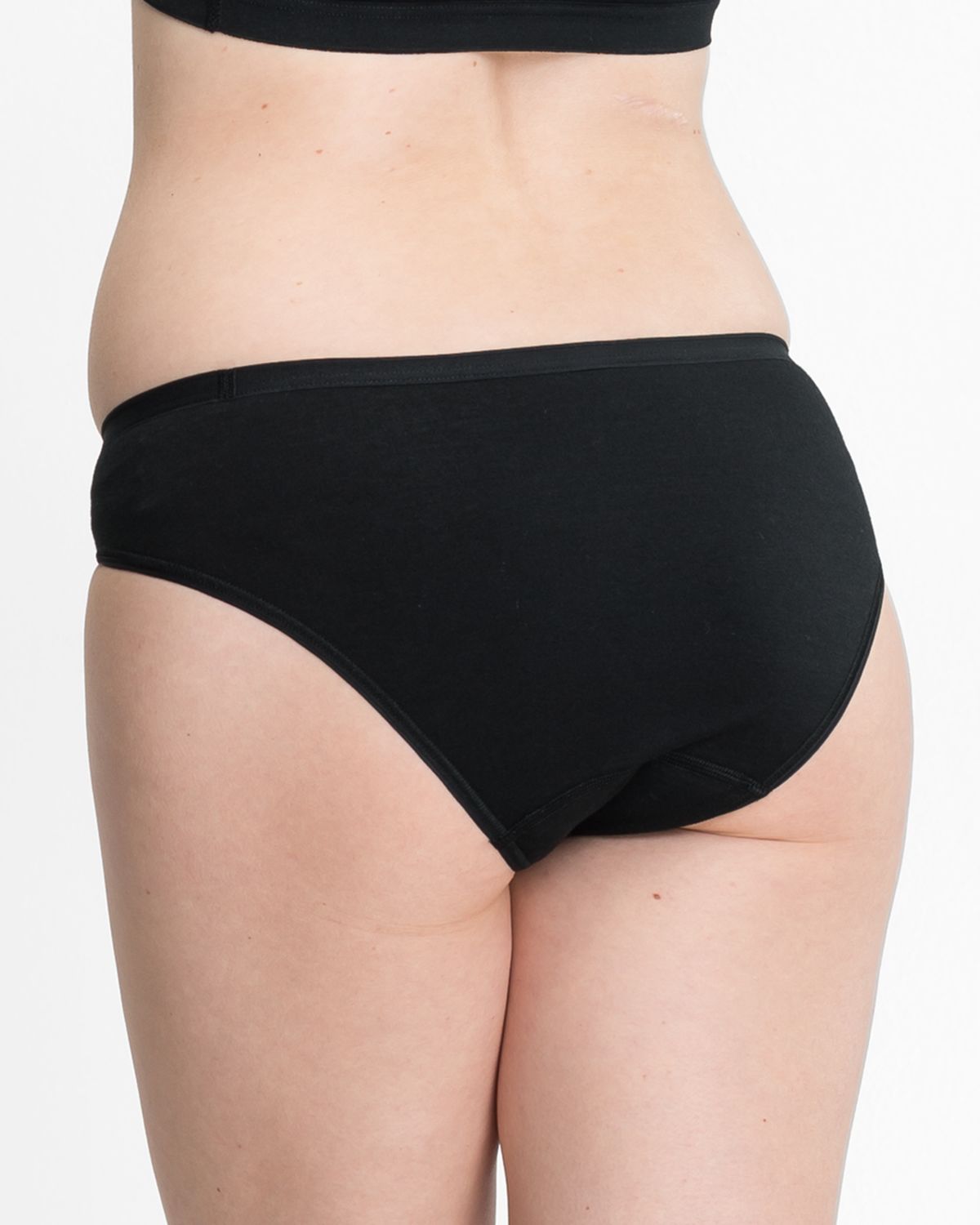 Model trägt Bikinislip in schwarz aus der Serie Bio Cotton plus, Ansicht von hinten.