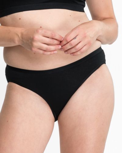 Model trägt Bikinislip in schwarz aus der Serie Bio Cotton plus, Ansicht von vorne.